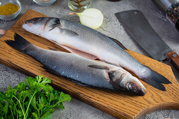 Raw fresh sea bass with different spices on cutting board