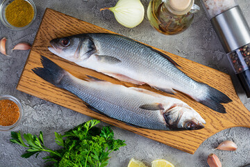 Raw fresh sea bass with different spices on cutting board. Top view