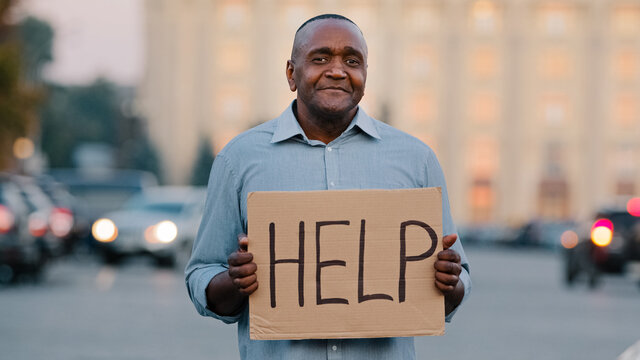 Unhappy Black African American Businessman Holding Cardboard With Text Help Emotional Pointing On Sign. Stressed Frustrated Man Hold Poster Looking For Job During Pandemic Talks About Himself Outdoor