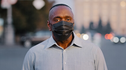 Adult mature african american man wearing black protective medical face mask posing outdoors. Elderly businessman standing on street during pandemic covid-19, virus protection, coronavirus epidemic  - Powered by Adobe