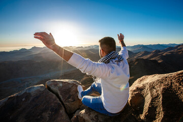 A man sits facing the rising sun with raised hands on Mount Sinai in Egypt.