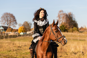Obraz premium Portrait of a mature woman in a steampunk costume on a horse against the backdrop of an autumn landscape.