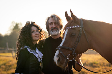 Obraz premium Portrait of a mature couple in a steampunk costume near a horse against the background of an autumn landscape.