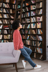 side view of african american woman leaning on grey couch near bookshelf