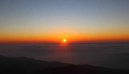 Sunrise seen from the mountains. Sun on the horizon above the clouds