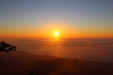 View from the top at sunrise in the mountains. Sun disk on the horizon above the clouds