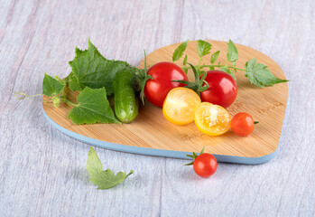 Young beautiful cherry tomatoes whole and sliced with beautiful young leaves and fresh beautiful cucumbers gherkins with leaves on a wooden cutting board
