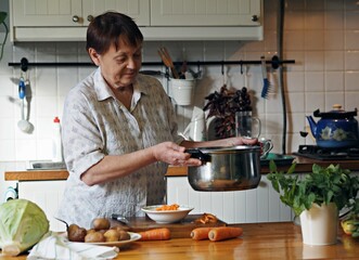 A retired woman in the kitchen prepares soup with ingredients spread on the table. Healthy homemade...