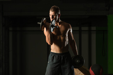 Close up dark portrait of a shirtless young man exercising dumbbell alternate biceps curl
