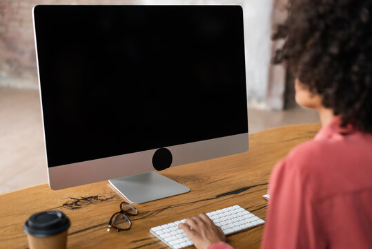 Back View Of Blurred African American Woman Typing On Computer Keyboard Near Blurred Paper Cup And Eyeglasses On Desk