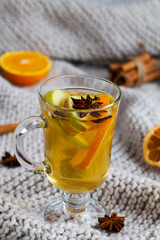 glass of Mulled drink on knitting plaid with copy space. Christmas hot white mulled wine in glass with honey, cinnamon sticks and star anise on light background. Spicy warm beverage.