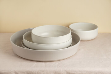 Scandinavian nordic style. Set of different modern white empty   ceramic tableware and glasses. Ceramic plates on white, flax rose tablecloth background. Overview empty food table with tableware