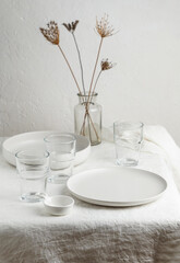 Scandinavian nordic style. Set of different modern white empty   ceramic tableware and glasses. Ceramic plates on white, flax rose tablecloth background. Overview empty food table with tableware