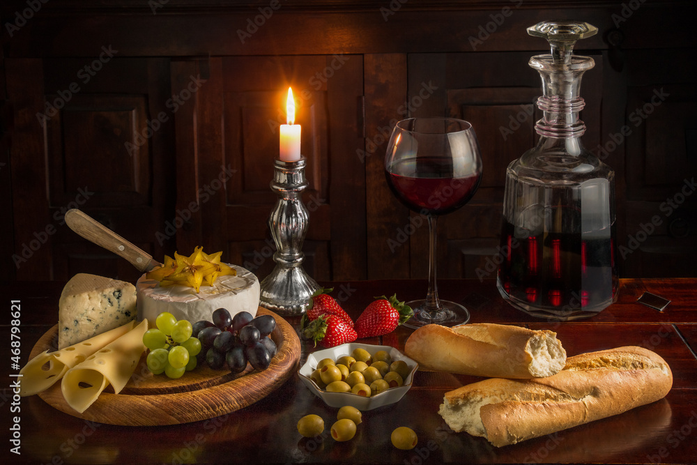 Poster Closeup of a dinner table with a bottle of wine, cheese, baguette and fruits.