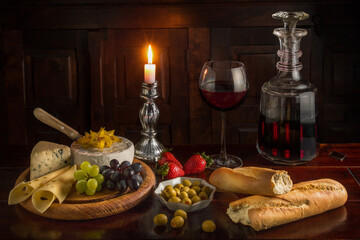 Closeup of a dinner table with a bottle of wine, cheese, baguette and fruits.