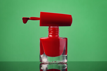 Red nail polish bottle and drop on brush on green background. Cosmetics concept.