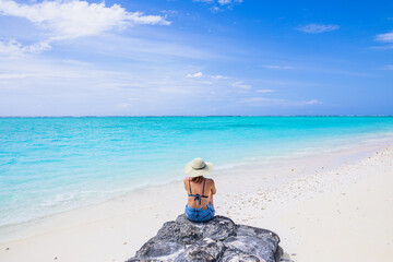 A girl in a straw hat sits alone on a Paradise beach on an island with turquoise water - Maldives