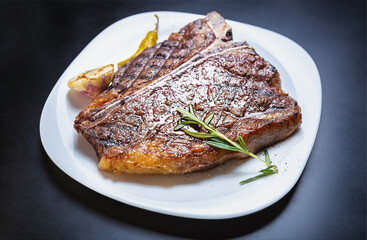Delicious t-bone steak meat cooked on grill for dinner in American restaurant. Gourmet beefsteak grilled and served on white plate with rosemary herb