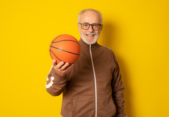 Mature sport man holding basketball isolated over yellow background.