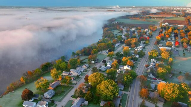 
Amazingly beautiful Fall neighborhood with colorful trees, next to river shrouded in fog at sunrise, aerial view. This scene is as surreal as it is breathtaking! A truly exceptional Autumn scenic.