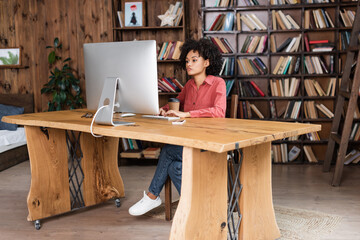 young african american woman typing on computer keyboard while looking at monitor at home