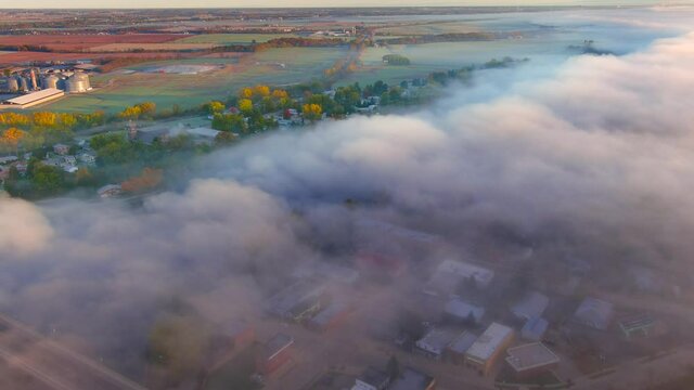 Amazingly beautiful Fall neighborhood with colorful trees, next to river shrouded in fog at sunrise, aerial view.