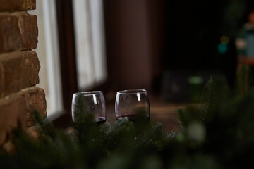 Glasses of wine in home Christmas atmosphere on the windowsill. Blurred foreground. Copy space. Low key festive card or backround