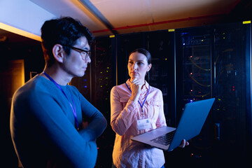Diverse male and female engineers using laptop in computer server room