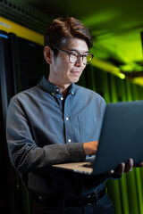 Asian male engineer using laptop in computer server room