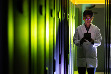 Asian male engineer wearing an apron using digital tablet while inspecting in computer server room