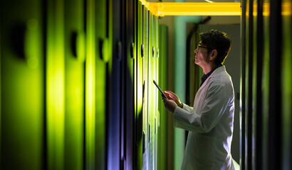 Asian male engineer wearing an apron using digital tablet while inspecting in computer server room