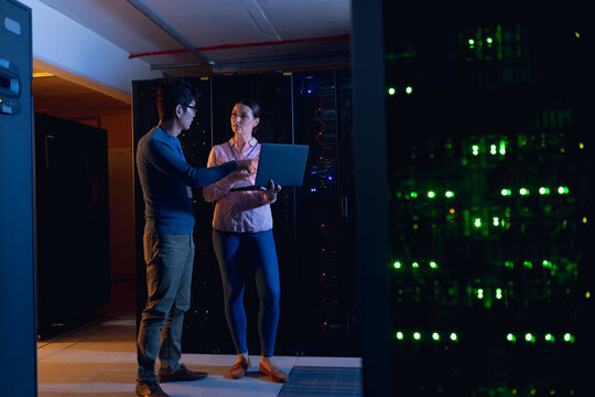 Diverse male and female engineers using laptop in computer server room