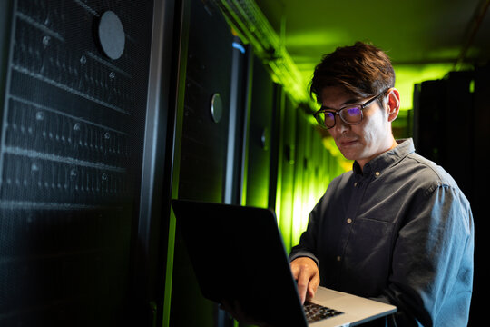 Asian male engineer using laptop in computer server room