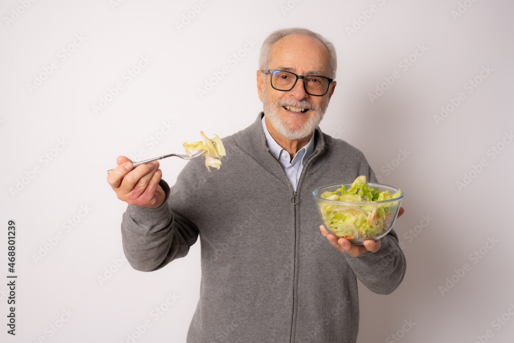 Wall mural senior happy man wearing casual sweater eating salad isolated over white background.