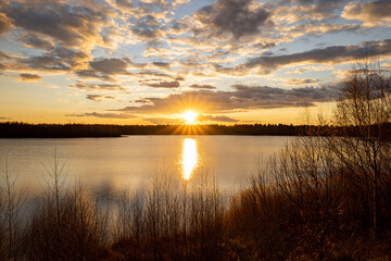 a beautiful blue lake with some tree silhouettes in the foreground under a dramatic sunset sky. High quality photo