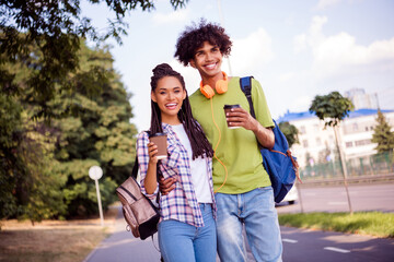 Photo of sweet cute boyfriend girlfriend wear casual outfits rucksacks headphones smiling walking drinking coffee outside urban city street