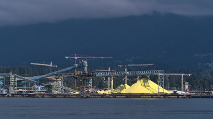 View of huge stock pile of bright yellow colored Sulphur (S) at bulk cargo terminal in North Vancouver, British Columbia, Canada with conveyor belts.