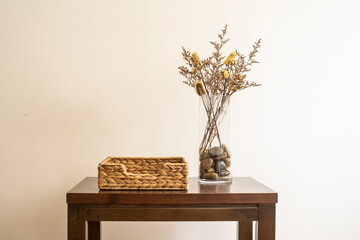Stylish modern dried flower arrangement in a glass vase with pebbles in it on a brown wooden table with a basket Boho style, morning sunlight in minimal home