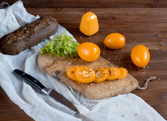 Whole yellow tomatoes and chopped on a wooden board, sprinkled with coarse salt, salad preparation
