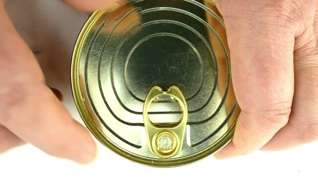 Hand opens metallic tin can of canned salmon in white sauce. Lifts the metal cover. Healthy canned food concept. Top view.