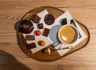 Plate with chocolates, a cup of coffee and a spoon on a wooden table