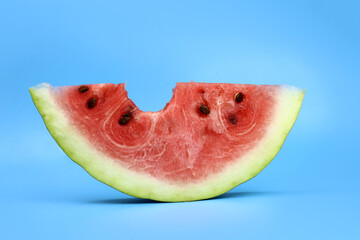 ripe red juicy watermelon slice bitten off on a blue background