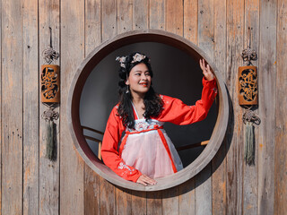 portrait of happy Asian woman tourist in red Hanfu ancient Chinese traditional ethnic costume looking out of wooden window 