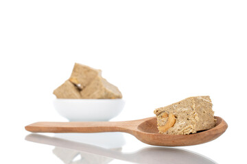 Three pieces of halva with peanuts on a white saucer with a wooden spoon, close-up, isolated on white.