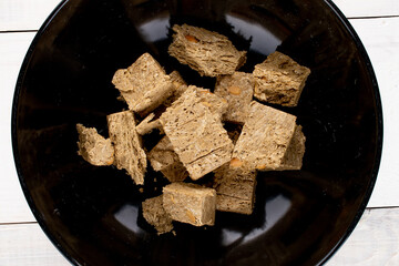 Several pieces of halva with peanuts on a black ceramic dish, close-up, top view.