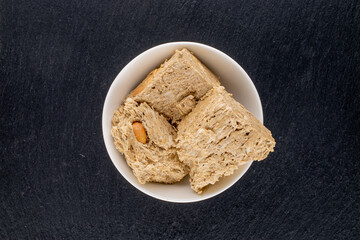 Three pieces of halva with peanuts with a white saucer on a slate stone, close-up, top view.