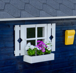 Blue play house with white shuttered window, window box flowers and Postal mailbox.