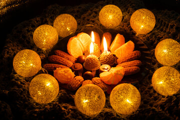 A Christmas plate with sweets, in the center there are three burning candles in the form of cones, around the included garland in the form of balls woven from threads. 