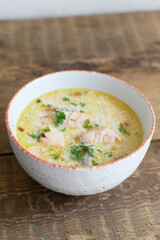 Salmon and cream fish soup in a white bowl on a wooden table. Lohikeitto is a traditional Finnish and Karelian soup. Rustic style. Horisontal orientation.