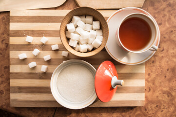Sugar and refined sugar with a cup of tea in a saucer on the table top view.